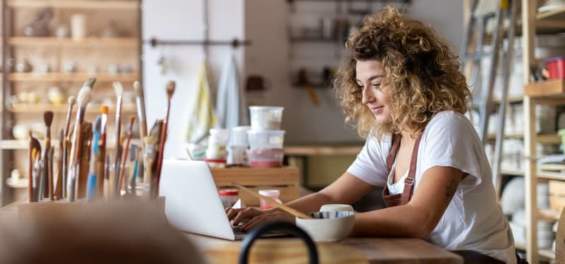 Woman pottery artist using laptop in art studio